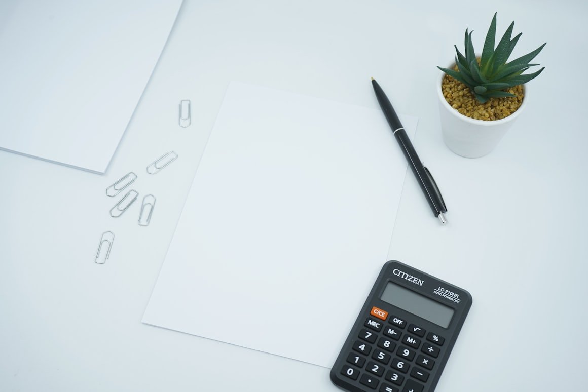Taschenrechner, Stift und Unterlagen auf einem aufgeräumten weißen Tisch